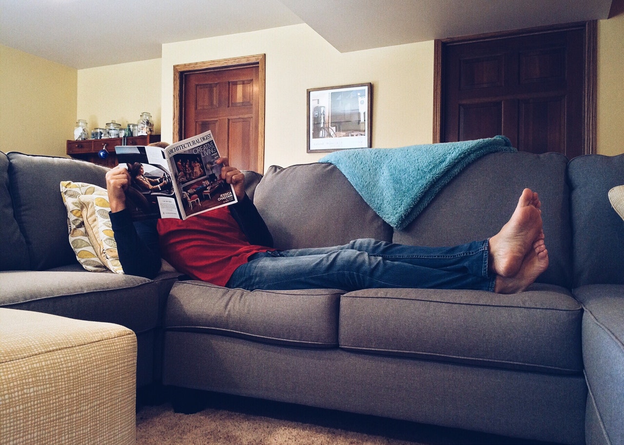 Person ligger på sovesofa med avis
